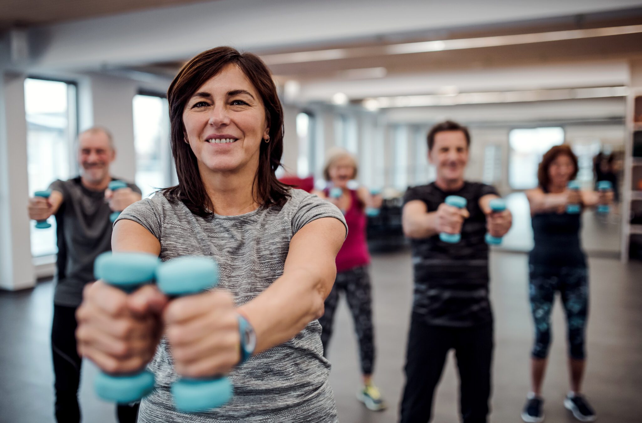 Group of cheerful seniors in gym doing exercise with dumbbells.