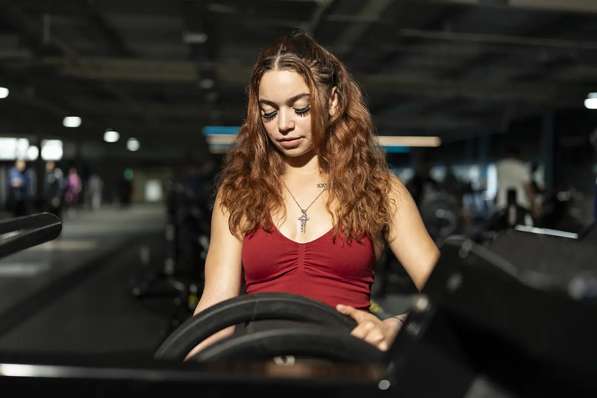 Woman looks down as she adjusts weights on a bar